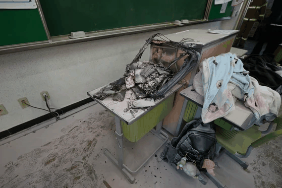 A burned phone storage box on a classroom desk, surrounded by scorched belongings