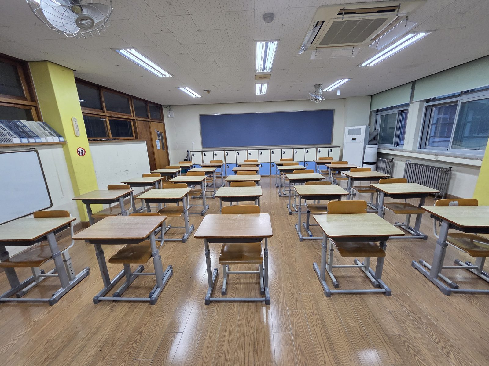 An empty Korean elementary classroom, desks in rows, lockers along the back wall — no phone tray or storage box anywhere in the room